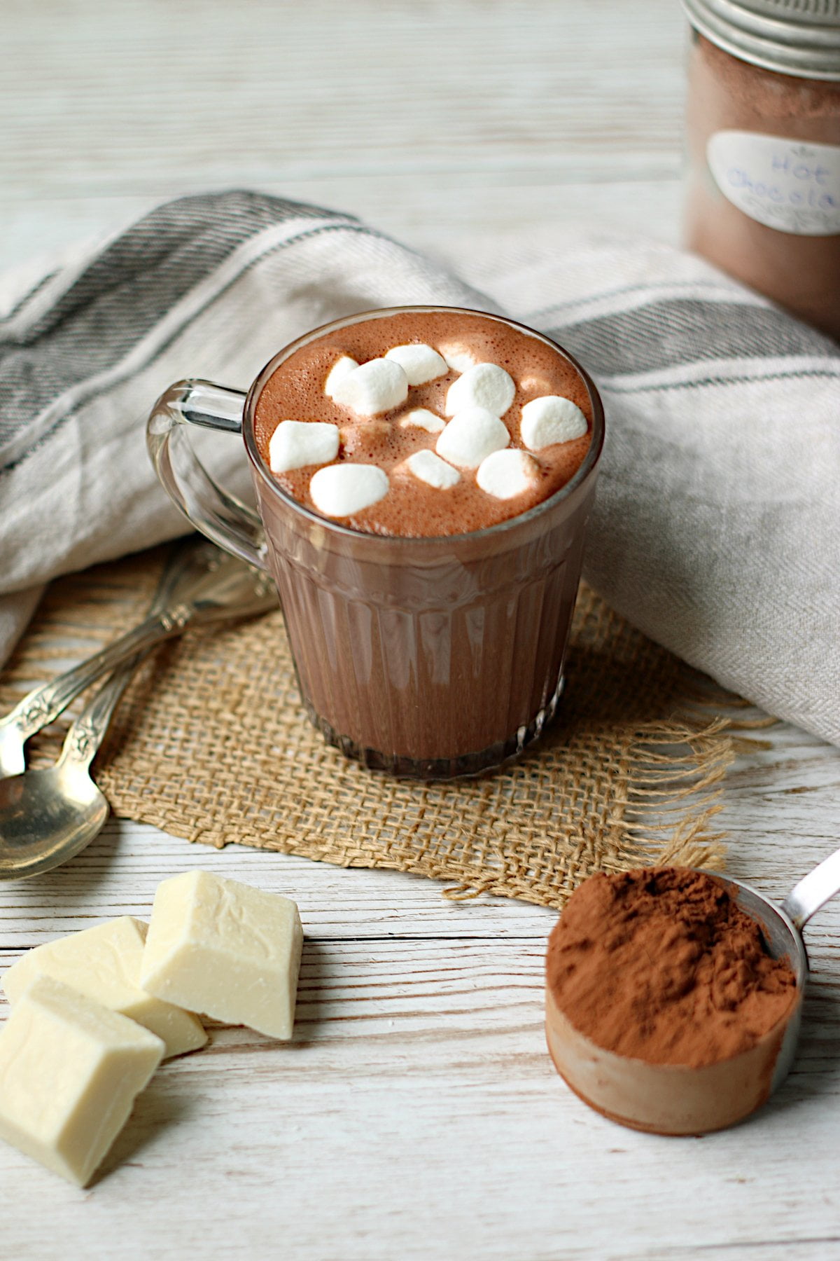 Homemade hot chocolate with mini marshmallows in a clear glass mug.