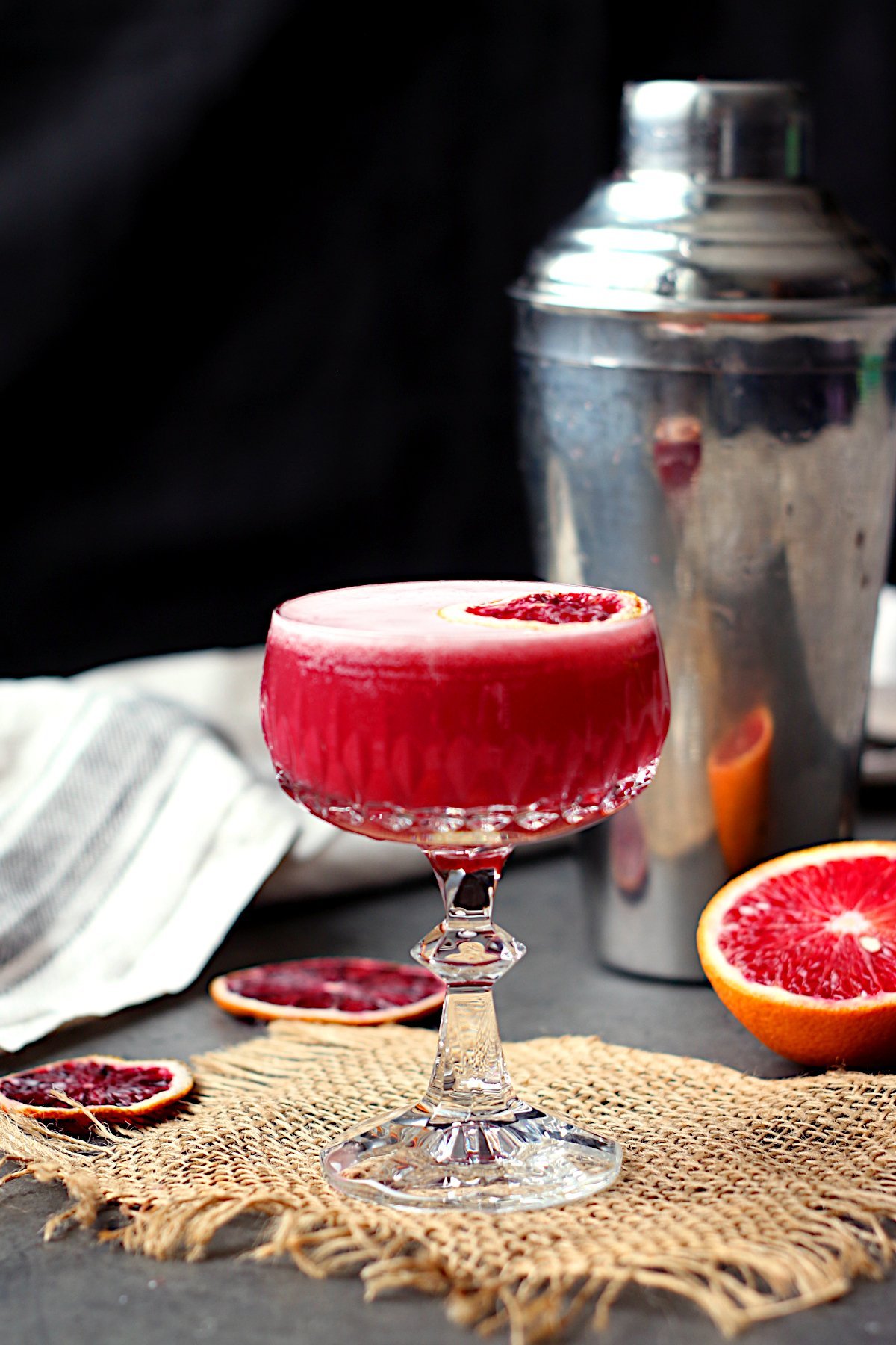 Blood orange whisky sour mocktail garnished with a dried blood orange slice in a crystal coupe glass.