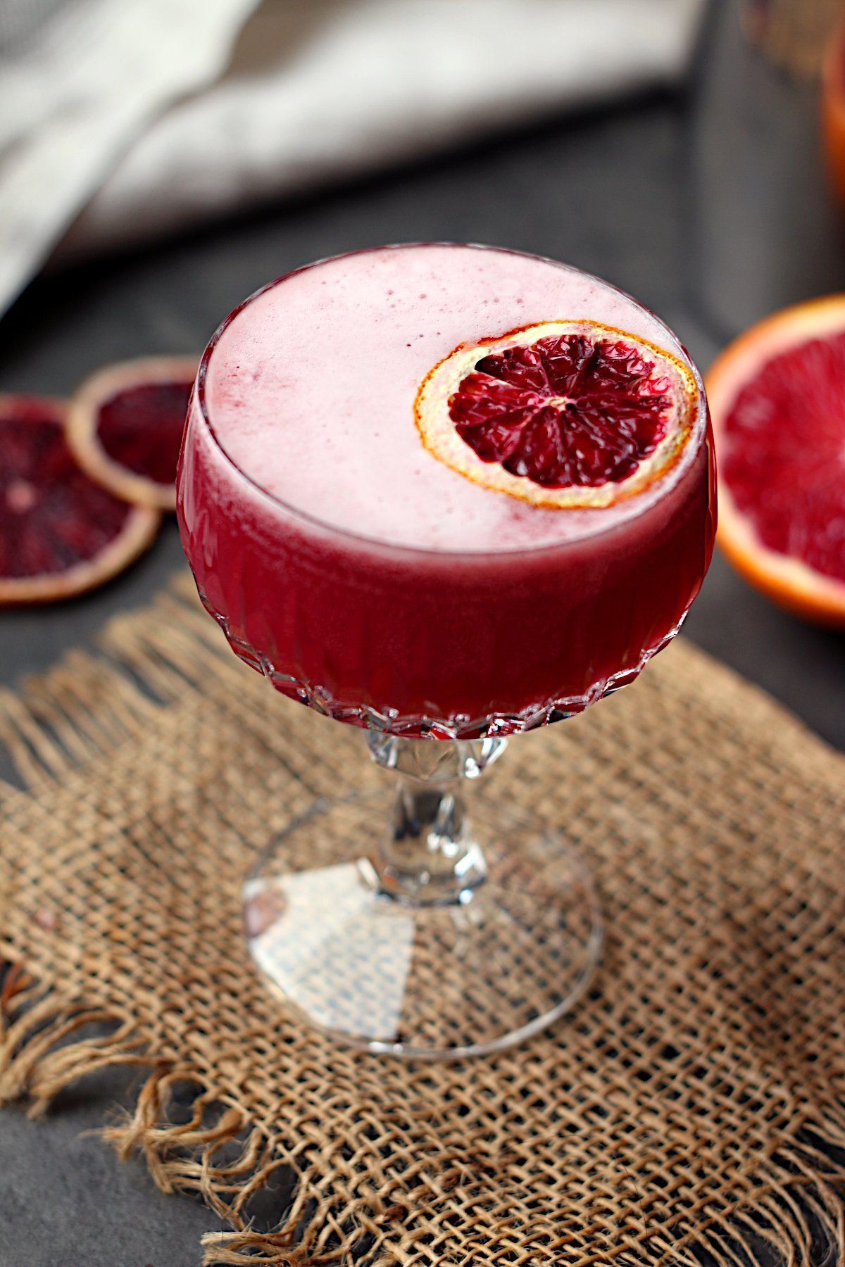Blood orange whisky sour mocktail garnished with a dried blood orange slice in a crystal coupe glass.
