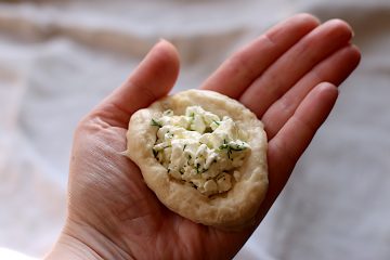 A hand holding a circle of dough stuffed with a cottage cheese dill filling.