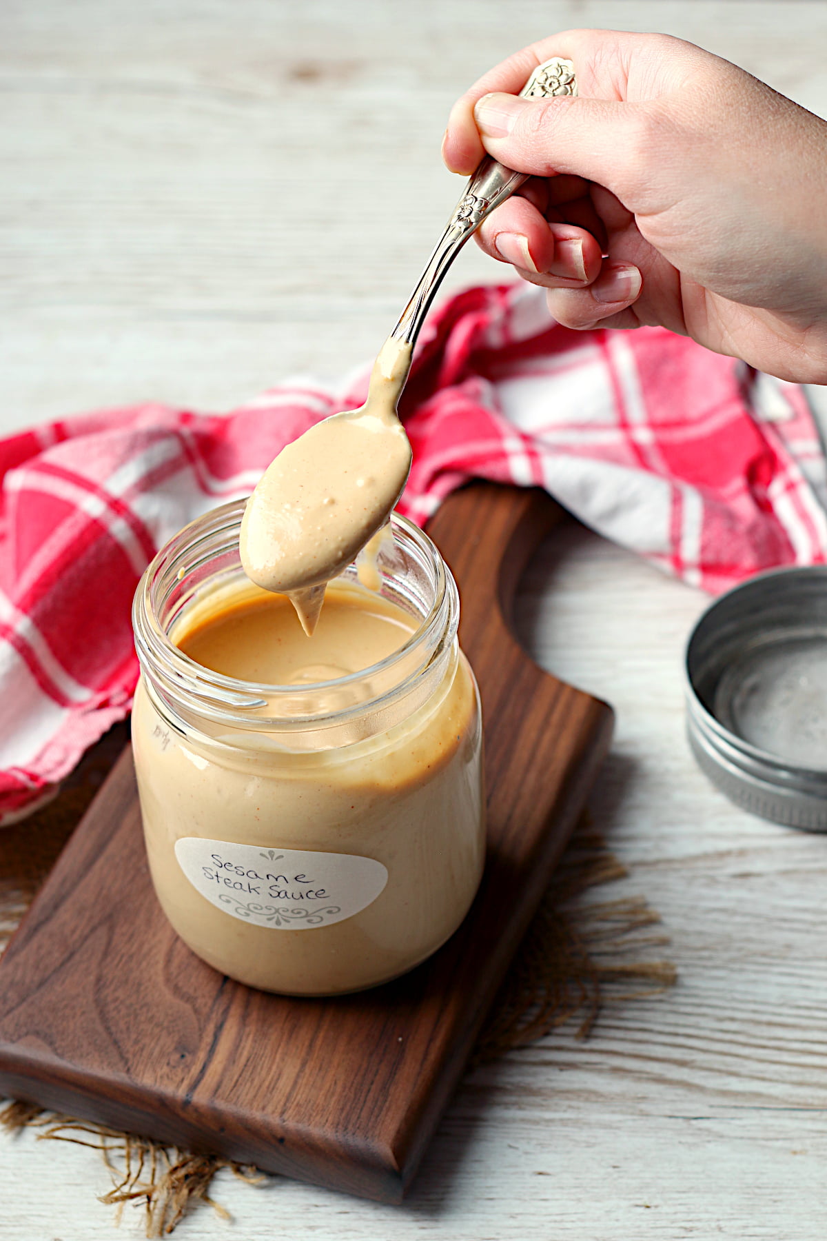 A spoon scooping a spooful of sesame steak sauce from a jar.