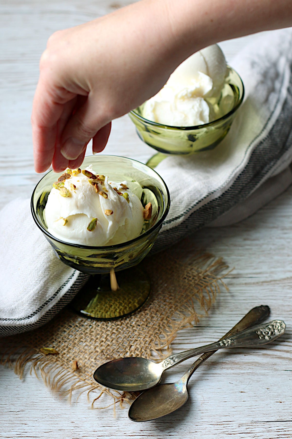 A hand sprinkling chopped pistachios on a small dish of Booza-Inspired Ice Cream.