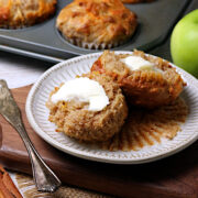 Two halves of an apple cheddar muffin with butter on a small white plate.