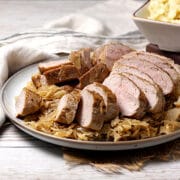 Sliced pork tenderloin sitting on a bed of sauerkraut on a large plate.
