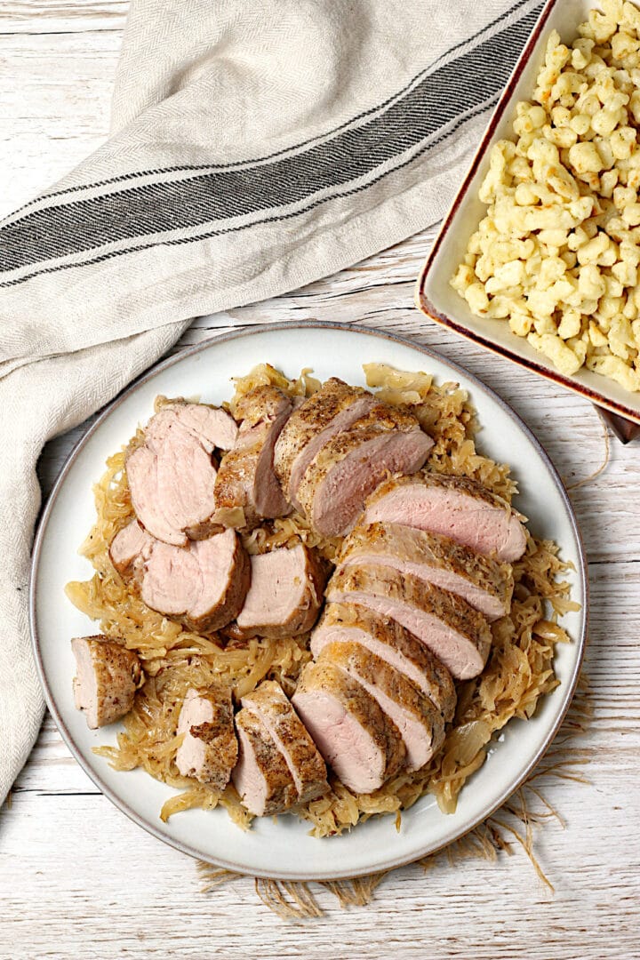 Domestic Dreamboat: Real, Easy, Food. Overhead photo of sliced pork tenderloin sitting on a bed of sauerkraut on a large plate.
