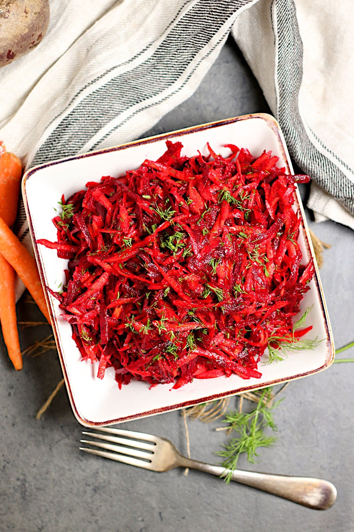 Overhead photo of Shredded Beet and Carrot Salad garnished with chopped dill in a square bowl.