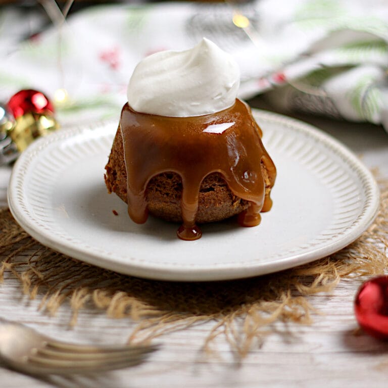 An individual sticky toffee pudding with a dollop of whipped cream on a small white plate.