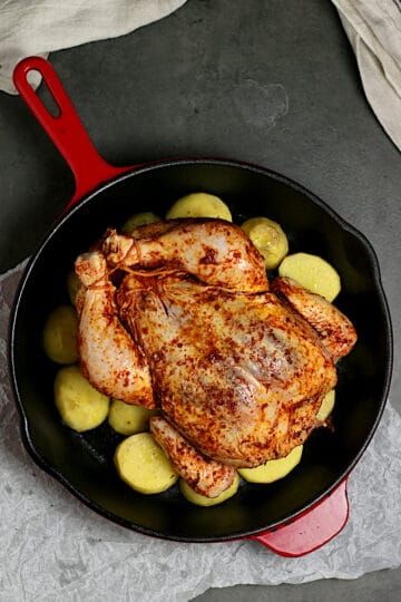 A whole chicken with smoked paprika rub and potatoes in a skillet before roasting.