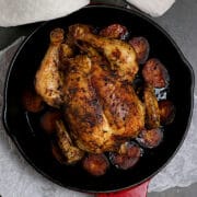 An overhead photo of a whole roasted chicken with potatoes in a red enamled cast-iron skillet.