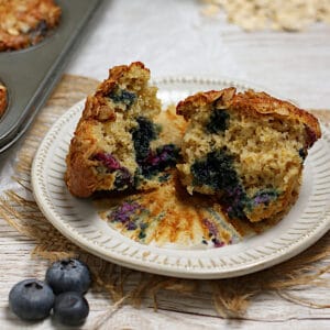 A blueberry oatmeal muffin broken into two pieces on a small white plate.