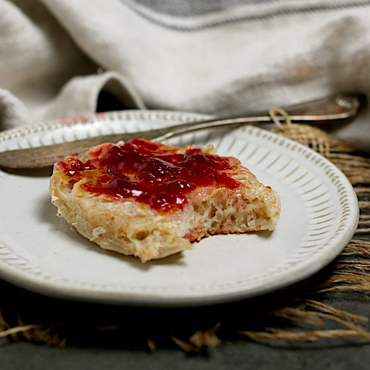 A Homemade Whole Wheat Crumpet with jam and a bite missing on a small white plate.