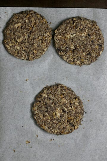 3 Uncooked Mushroom Grain Burger patties on a parchment-lined baking sheet.