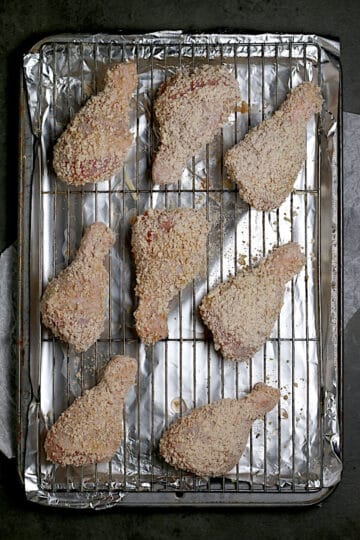 Breaded chicken drumsticks on a baking sheet before cooking.