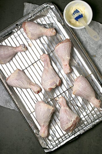 Mayonnaise-brushed chicken drumsticks on a baking sheet.