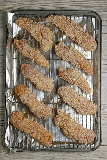 Uncooked oven-baked chicken tenders on a baking sheet.