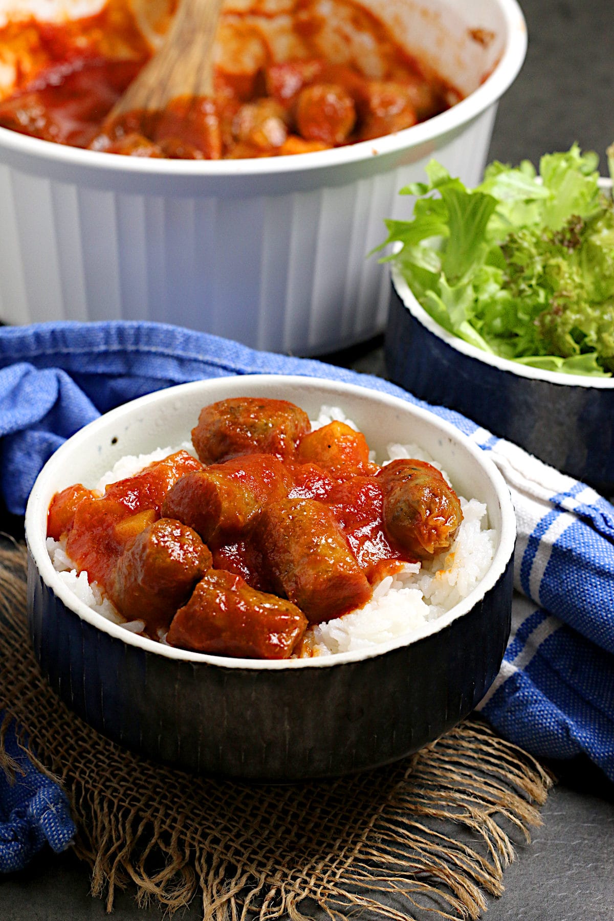 Peachy Sweet and Sour Sausages Peachy Sweet and Sour Sausages over white rice in a black bowl.