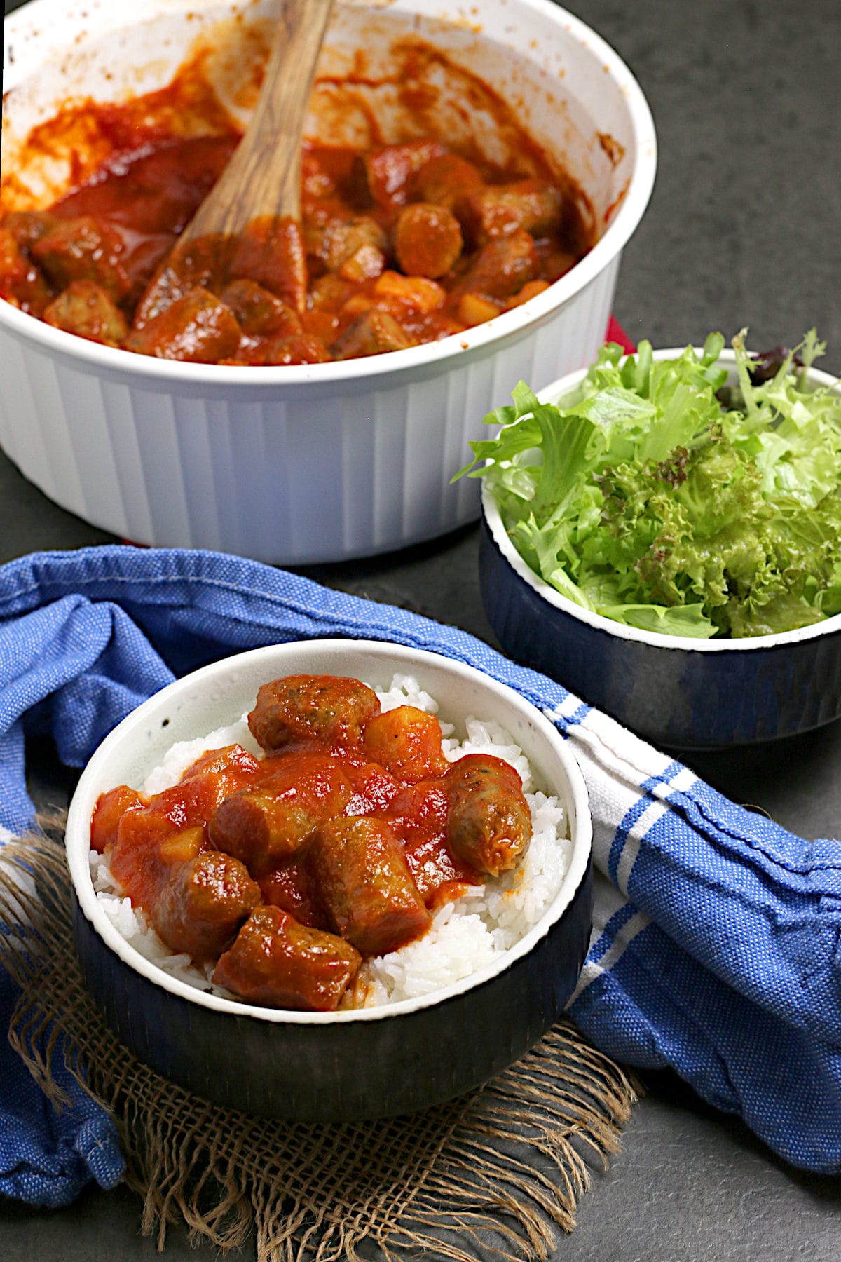 Peachy Sweet and Sour Sausages Peachy Sweet and Sour Sausages over white rice in a black bowl.