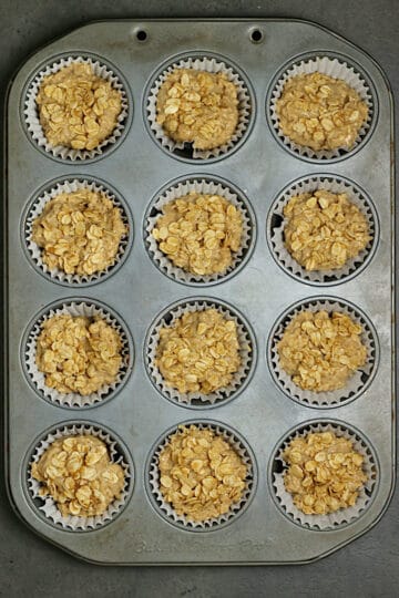 Maple and Brown Sugar Oatmeal Muffin Batter topped with oat crumble topping in a muffin pan before baking.