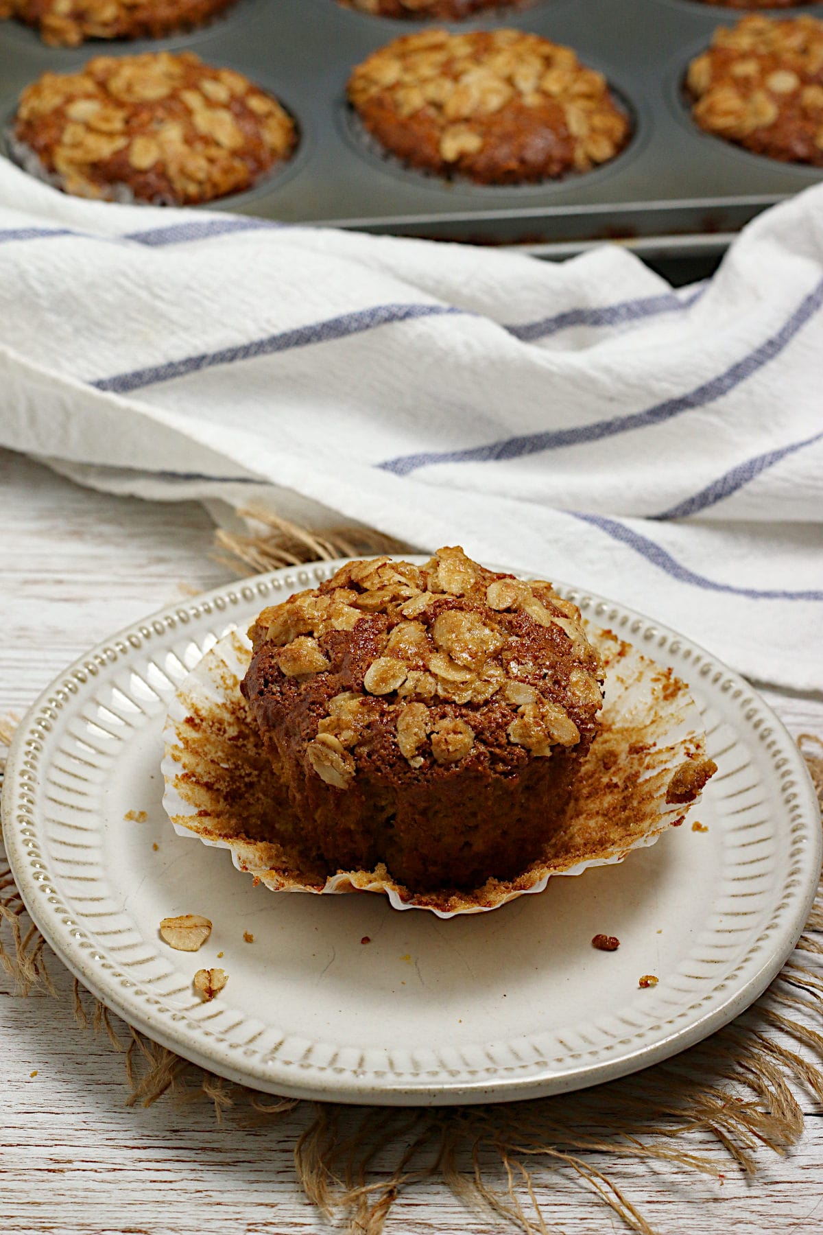Maple and Brown Sugar Oatmeal Muffins A homemade Maple and Brown Sugar Oatmeal Muffin with it's paper wrapper peeled off on a small white plate.