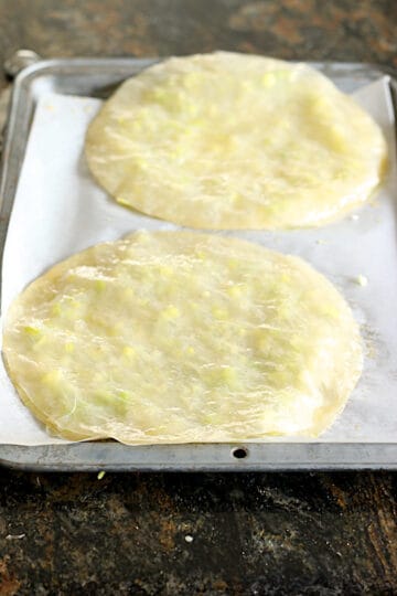 Two uncooked Rice Paper Green Onion Cakes on a parchment-lined baking sheet.