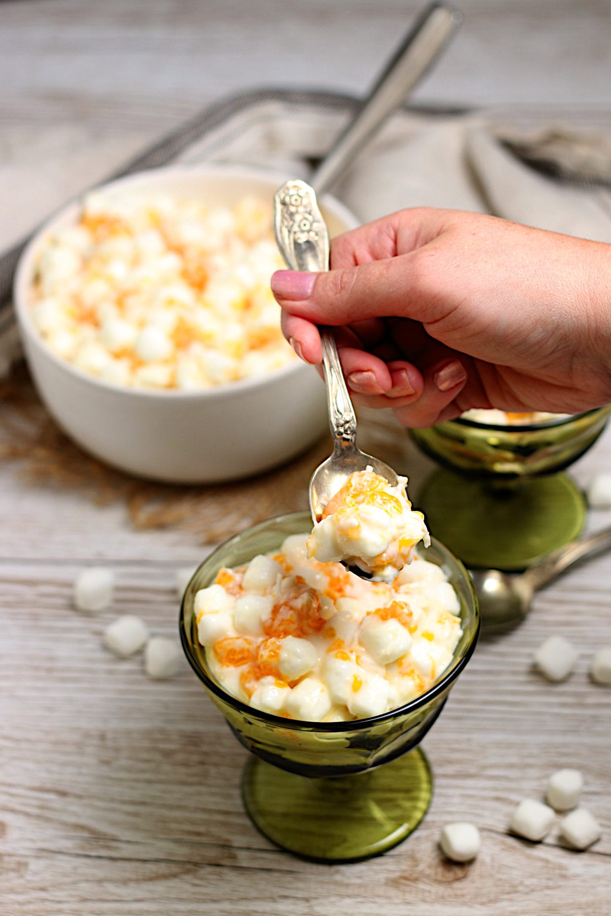 A hand scooping a spoonful of Orange Dream Ambrosia from a green dessert cup.