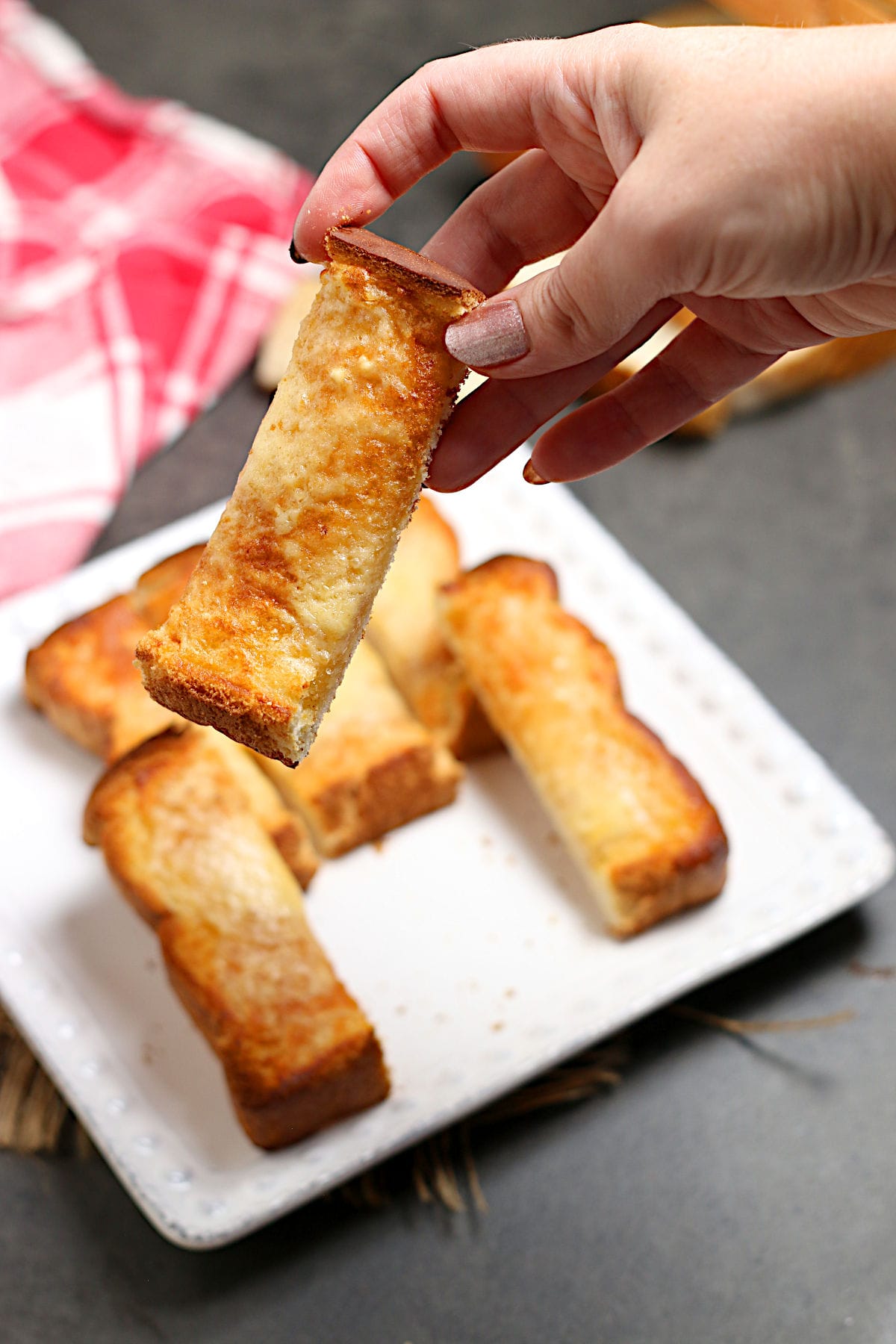 A hand holding a slice of three cheese toast.