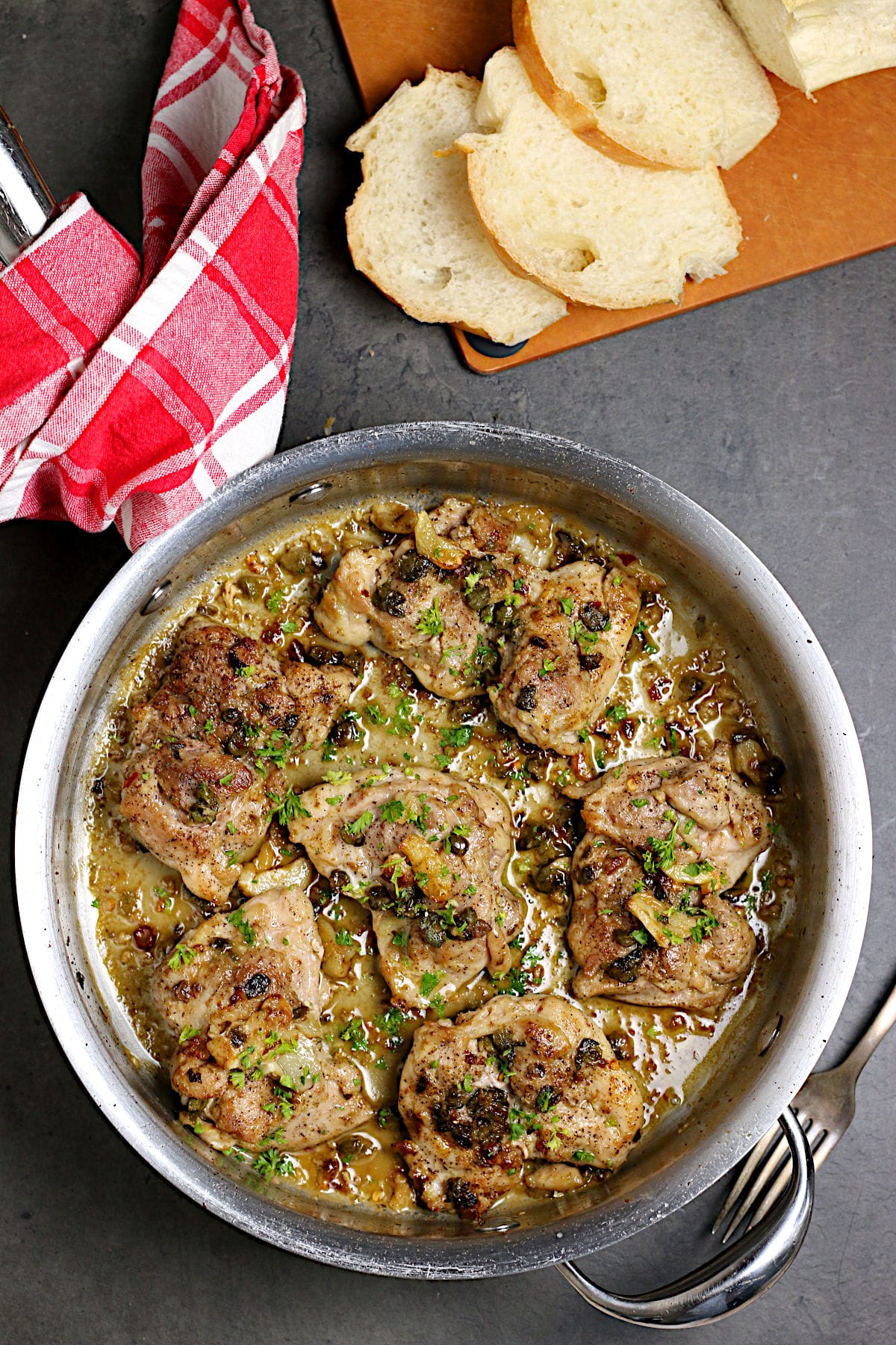 Overhead photo of chicken thighs with anchovies and capers in a saute pan.