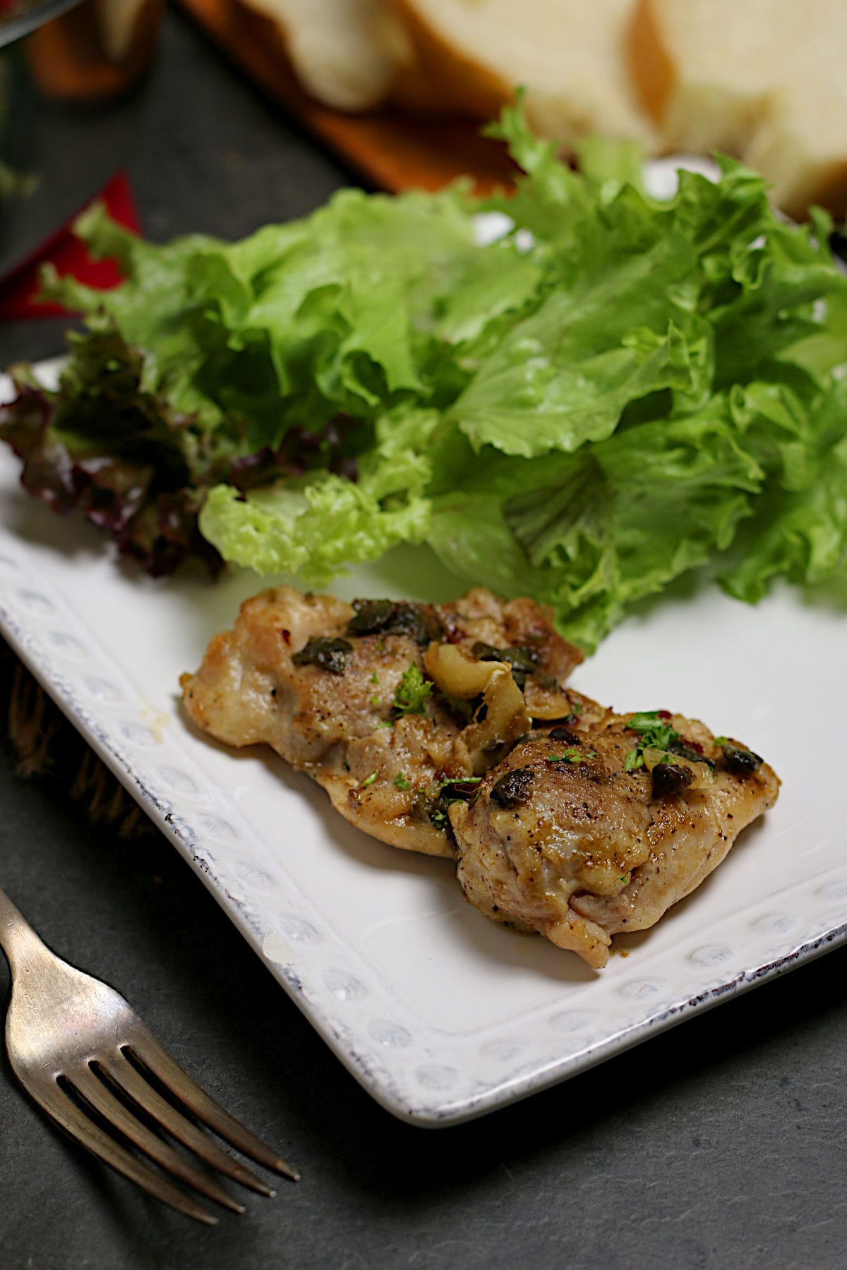 Closeup photo of Chicken Thigh with Anchovies and Capers with salad on a white plate.