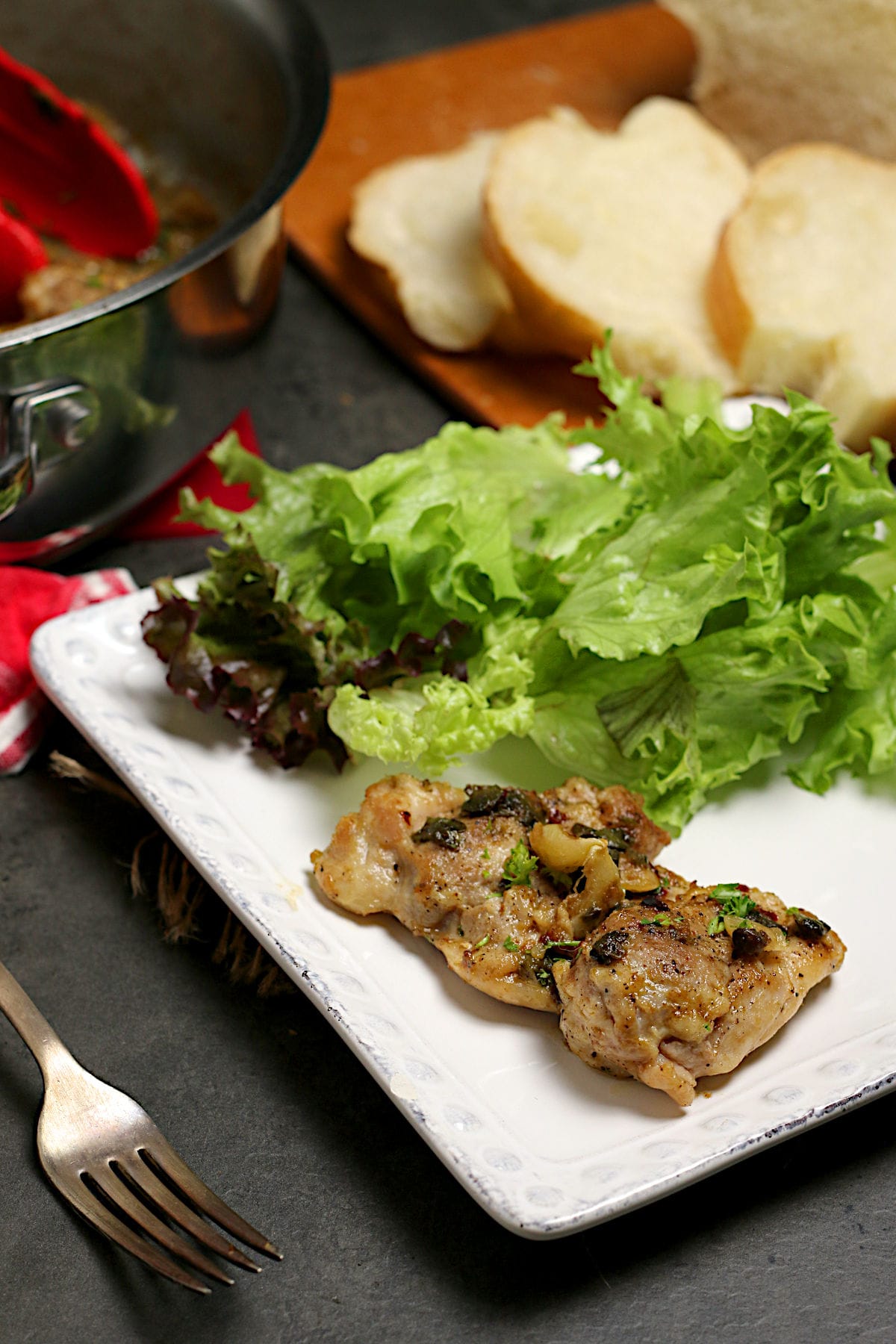 Chicken Thigh with Anchovies and Capers with salad on a white plate.