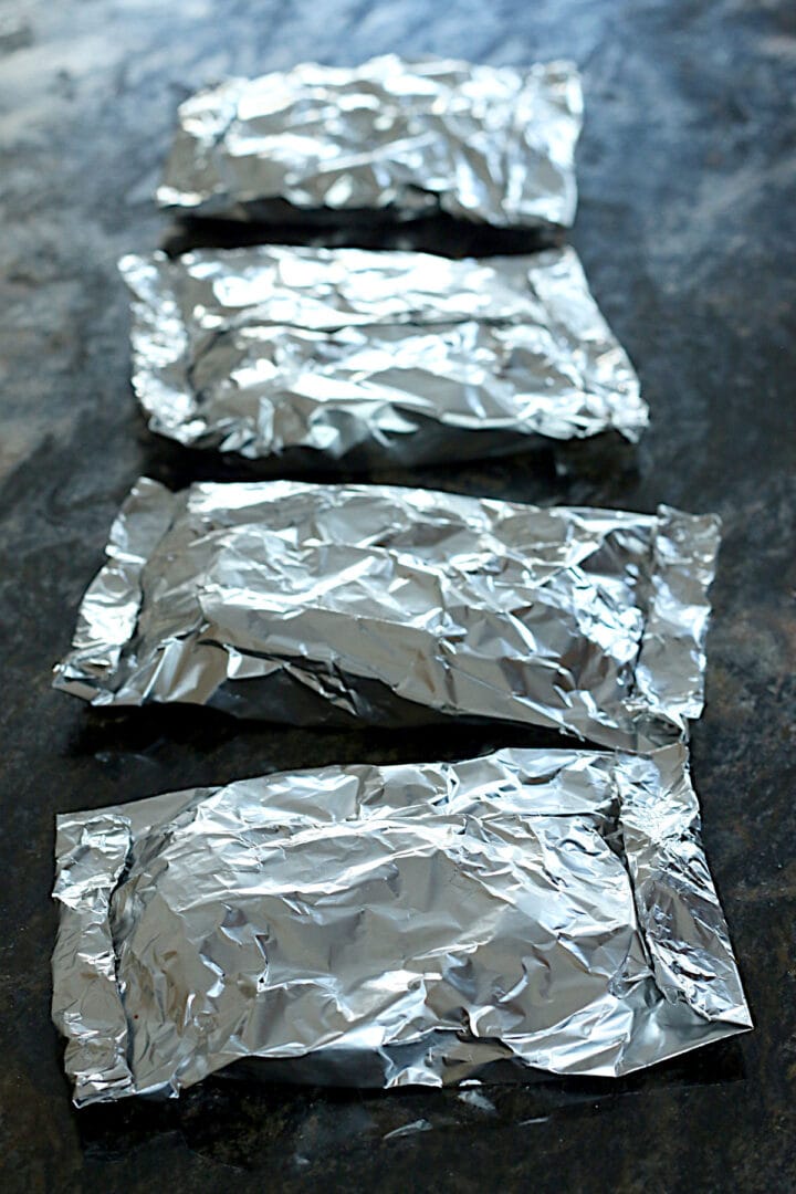 Four aluminum foil packets containing potatoes.