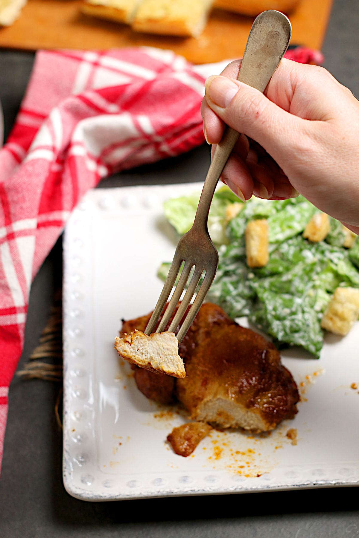 A hand holding a fork with a piece of Hot Honey Glazed Chicken Thigh on it.