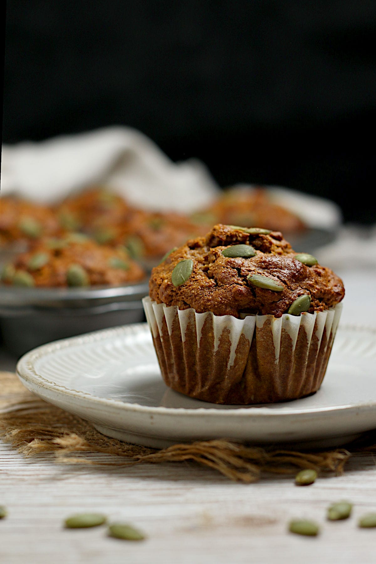 An Oatmeal Pumpkin Spice Muffin topped with pumpkin seeds on a small white plate.