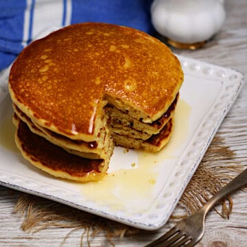 A stack of cornmeal pancakes with honey butter syrup with a wedge cut out of them.