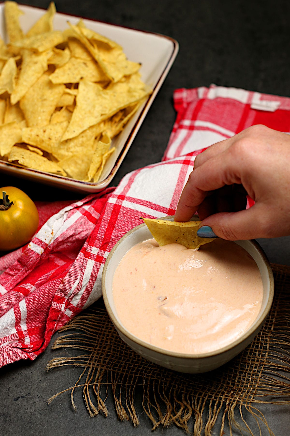 A hand dipping a tortilla chip in Cottage Cheese Queso.