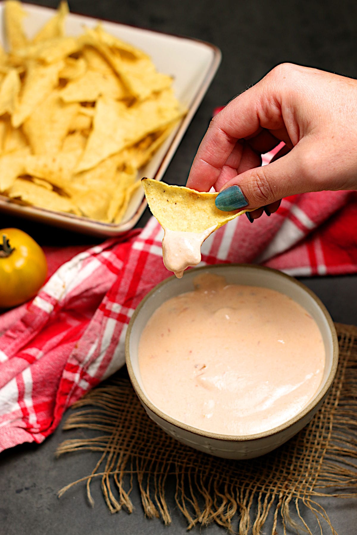 A hand holding a tortilla chip dipped in Cottage Cheese Queso.