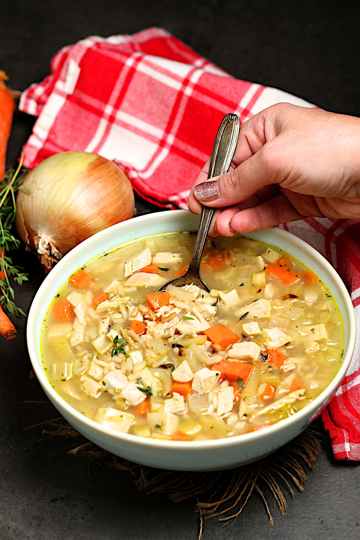 A hand scooping a spoonful of Turkey Rice Soup from a pale blue bowl.