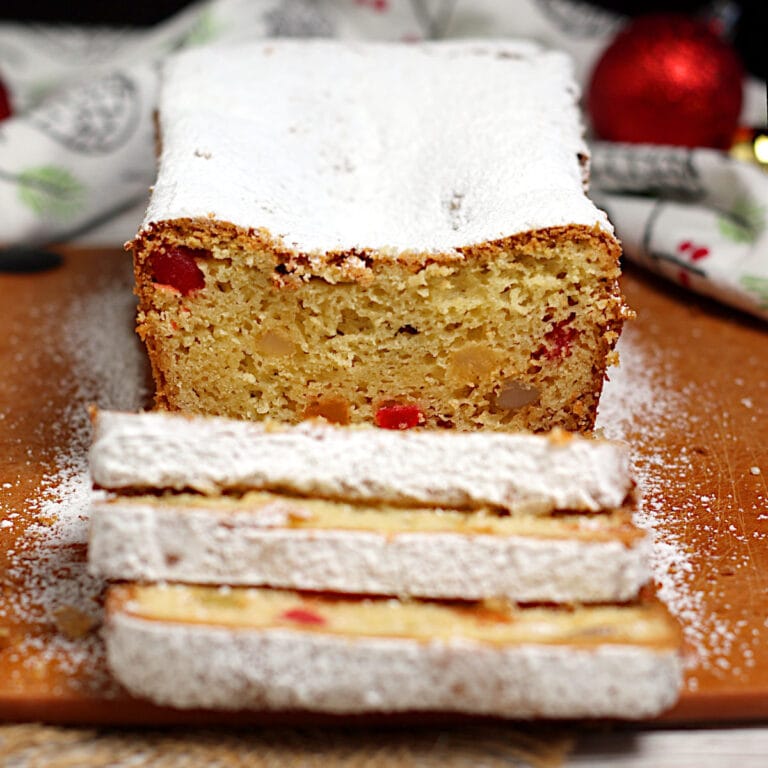 A Gumdrop Loaf Cake topped with powdered sugar on a cutting board.