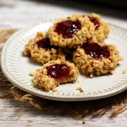 A stack of Raspberry Walnut Thumbprint Cookies on a small white plate.