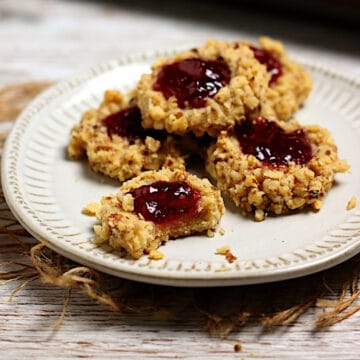 A stack of Raspberry Walnut Thumbprint Cookies on a small white plate.