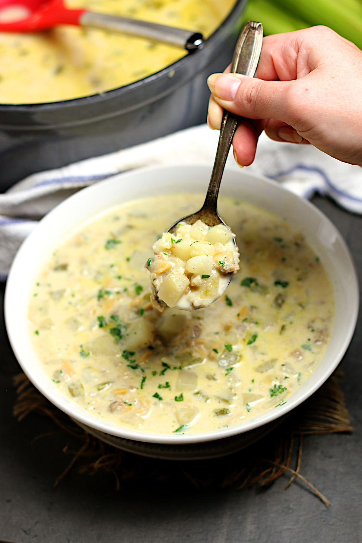 A hand holding a spoonful of New England Clam Chowder Soup.