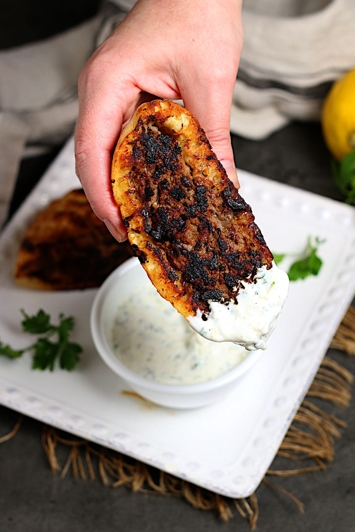 A hand holding a Lebanese Araye dipped in Lemon Yogurt Sauce.