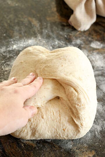 A hand folding sourdough on a lightly floured countertop.