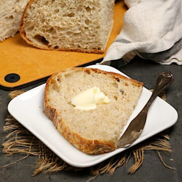 A slice of County-Style Sourdough Bread with butter on a small white plate.