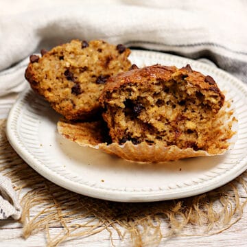 An Oatmeal Chocolate Chip Muffin broken in half on a small white plate.