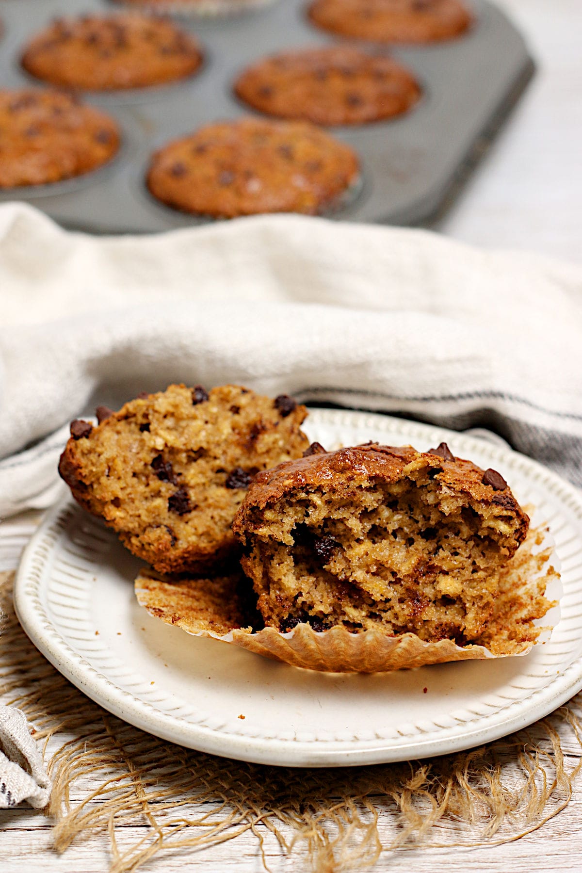 An Oatmeal Chocolate Chip Muffin broken in half on a small white plate.