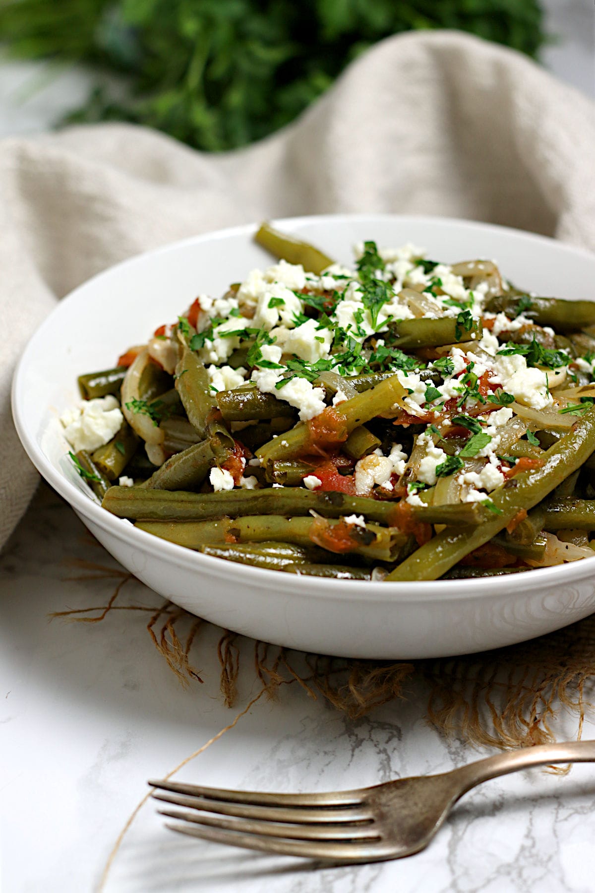 A closeup photo of Greek-Style Green Beans in a white bowl.