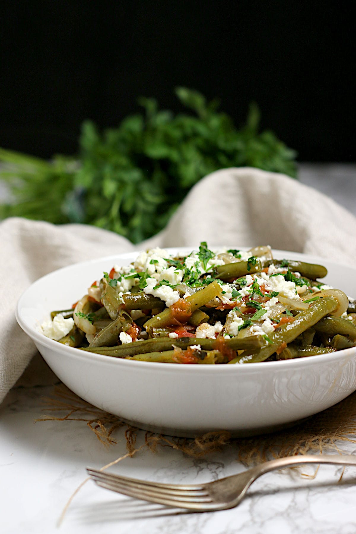 A closeup photo of Greek-Style Green Beans in a white bowl.
