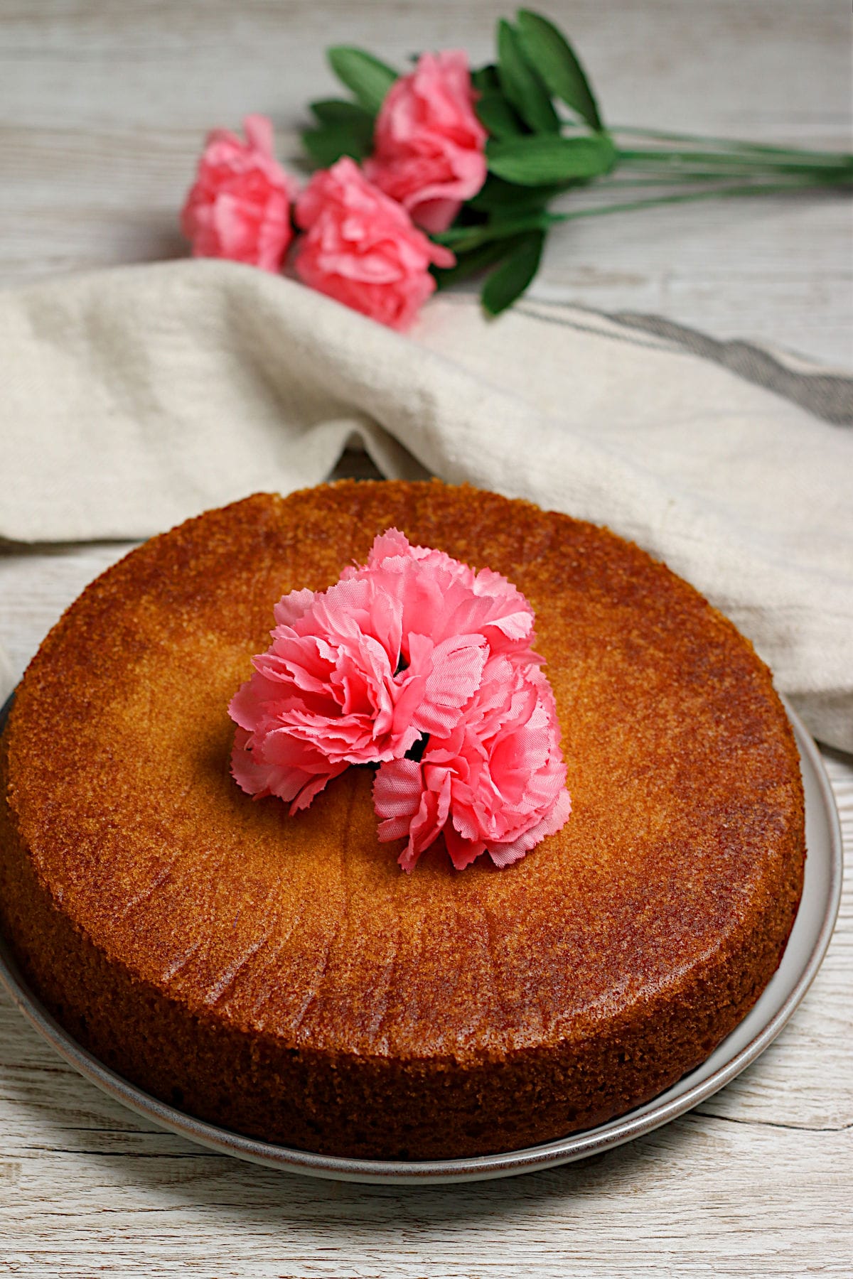 A whole honey rose cake decorated with pink flowers.