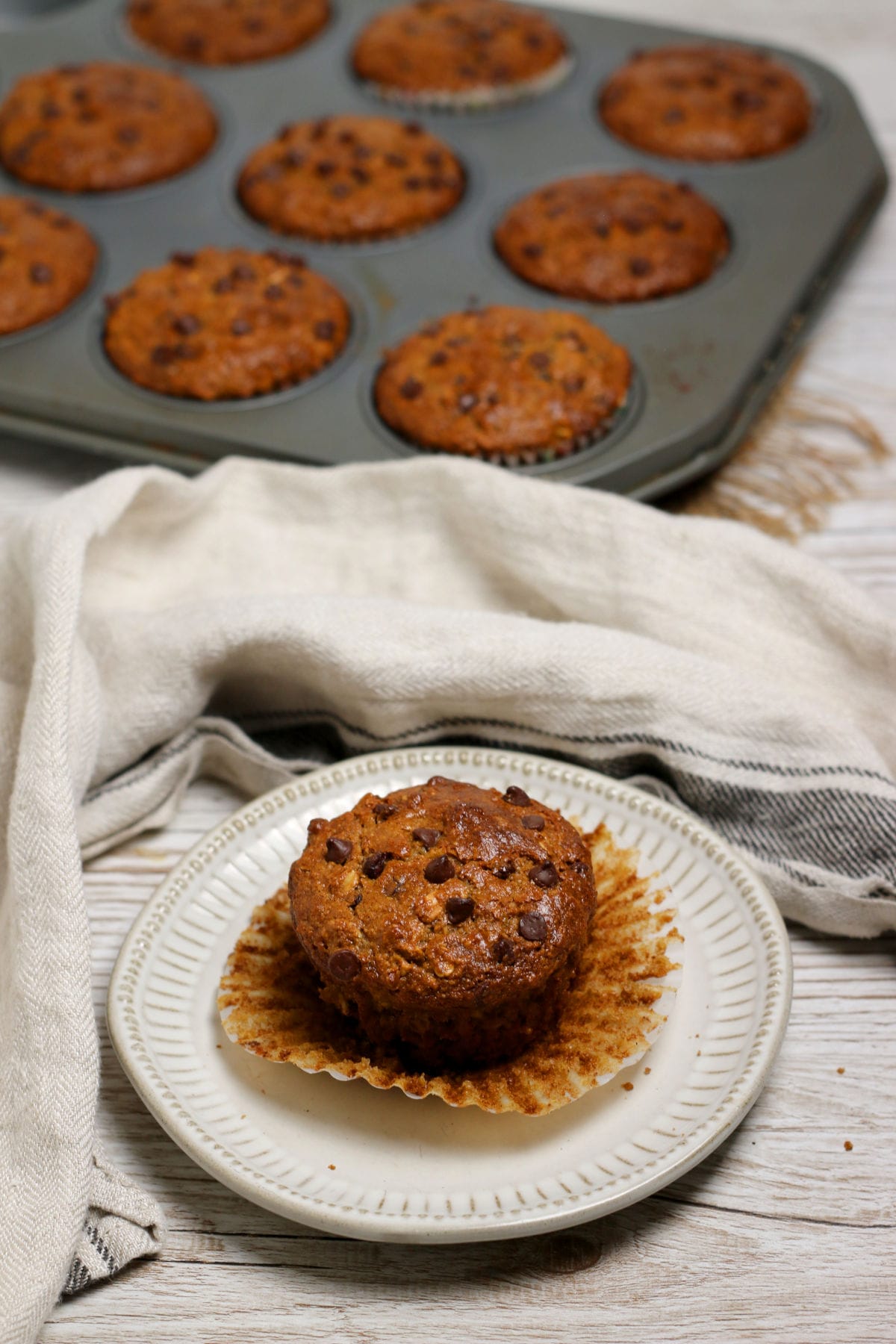 An unwrapped Oatmeal Chocolate Chip muffin on a small white plate.
