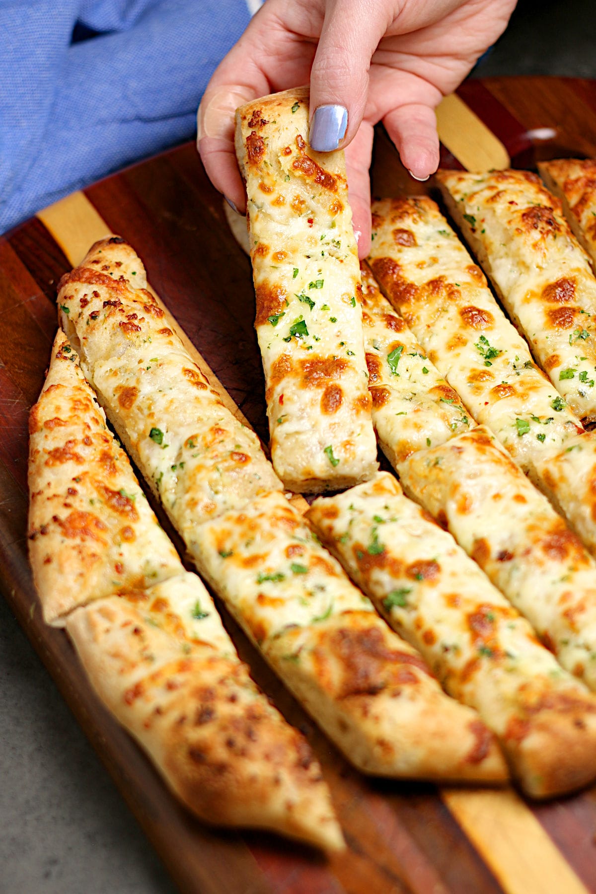 A hand picking up a piece of Nova Scotia Garlic Fingers from a cutting board.